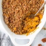 A bird's-eye view of a sweet potato casserole in a casserole dish with a serving spoon scooping out some sweet potato filling