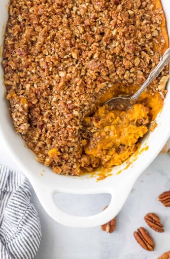 A bird's-eye view of a sweet potato casserole in a casserole dish with a serving spoon scooping out some sweet potato filling