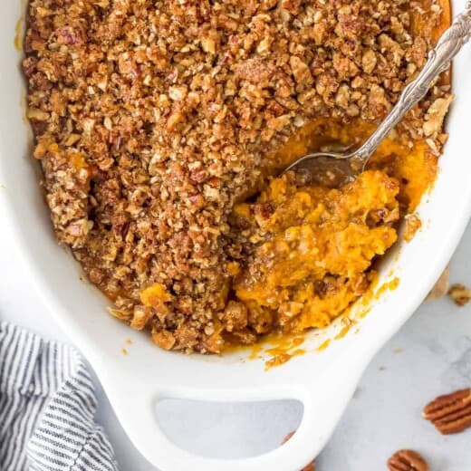 A bird's-eye view of a sweet potato casserole in a casserole dish with a serving spoon scooping out some sweet potato filling