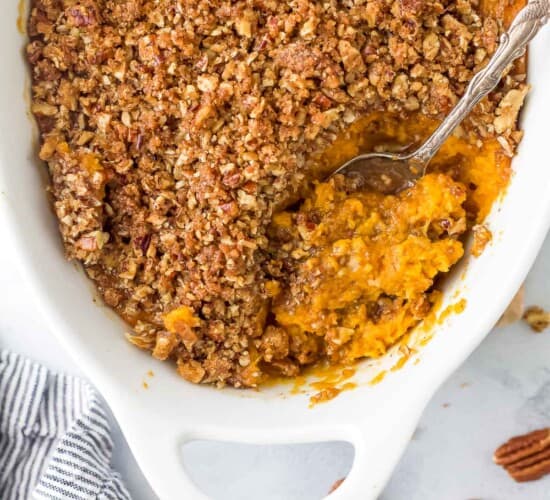 A bird's-eye view of a sweet potato casserole in a casserole dish with a serving spoon scooping out some sweet potato filling