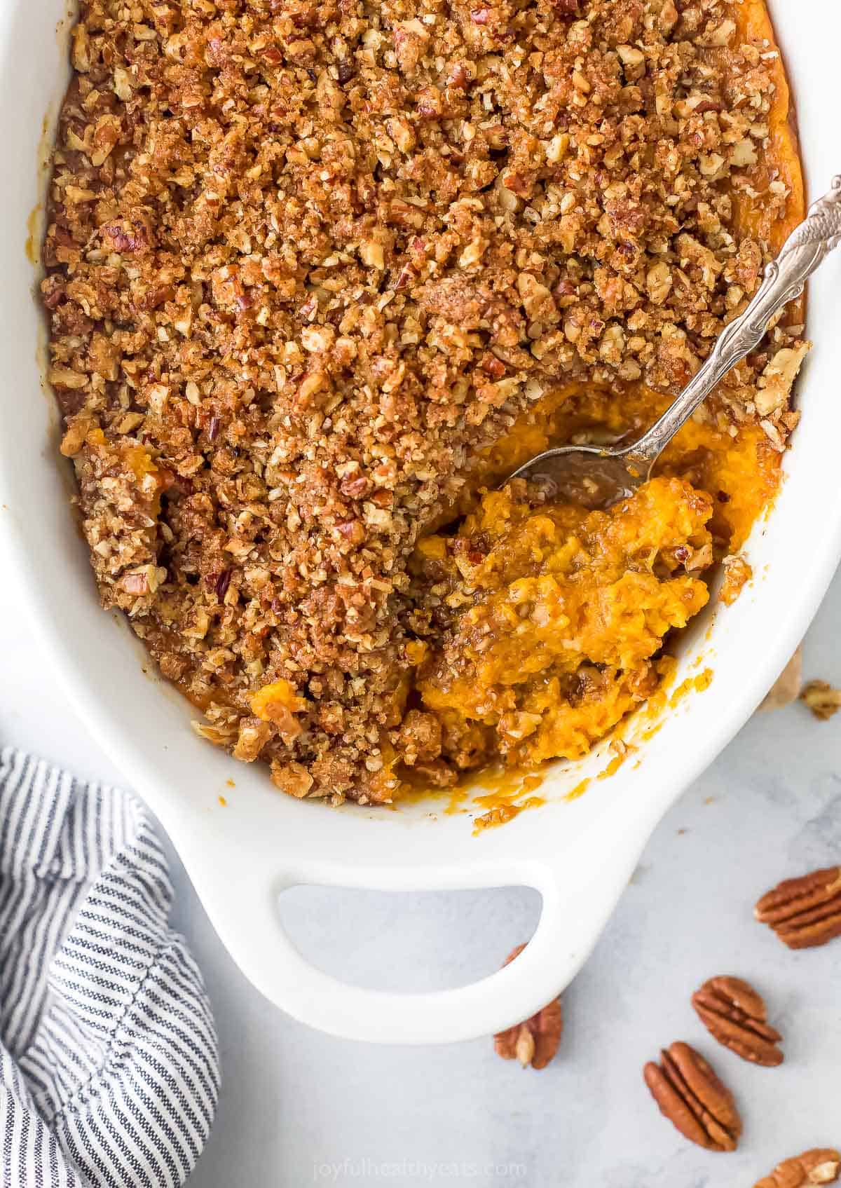 A bird's-eye view of a sweet potato casserole in a casserole dish with a serving spoon scooping out some sweet potato filling