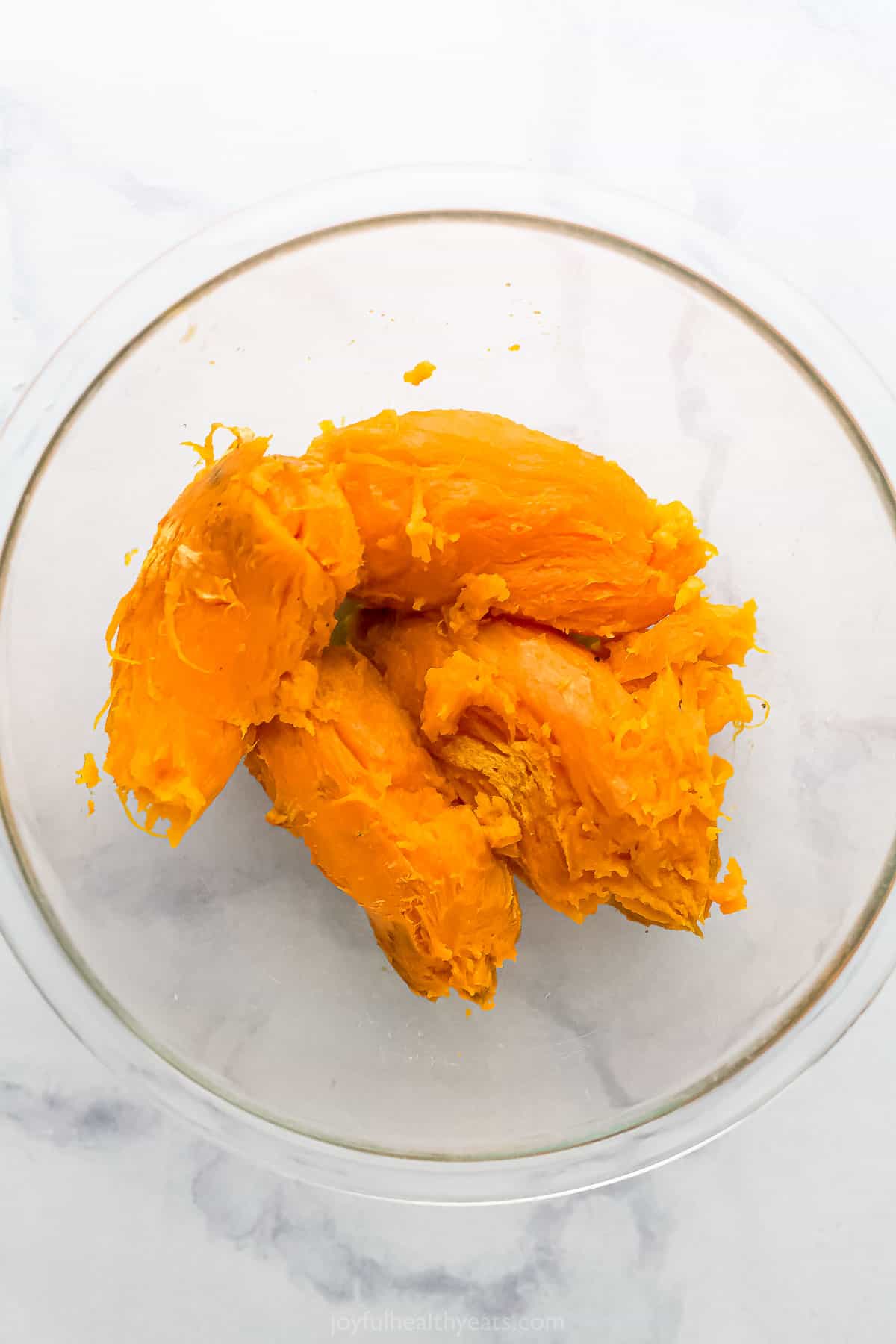 Four baked and peeled sweet potatoes inside of a large glass mixing bowl