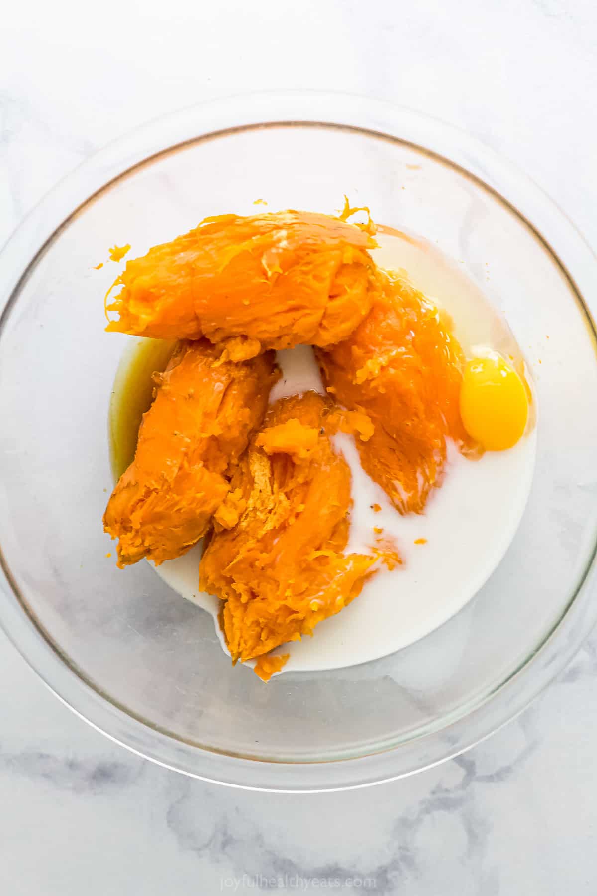 Baked and peeled sweet potatoes in a glass bowl with milk and an egg