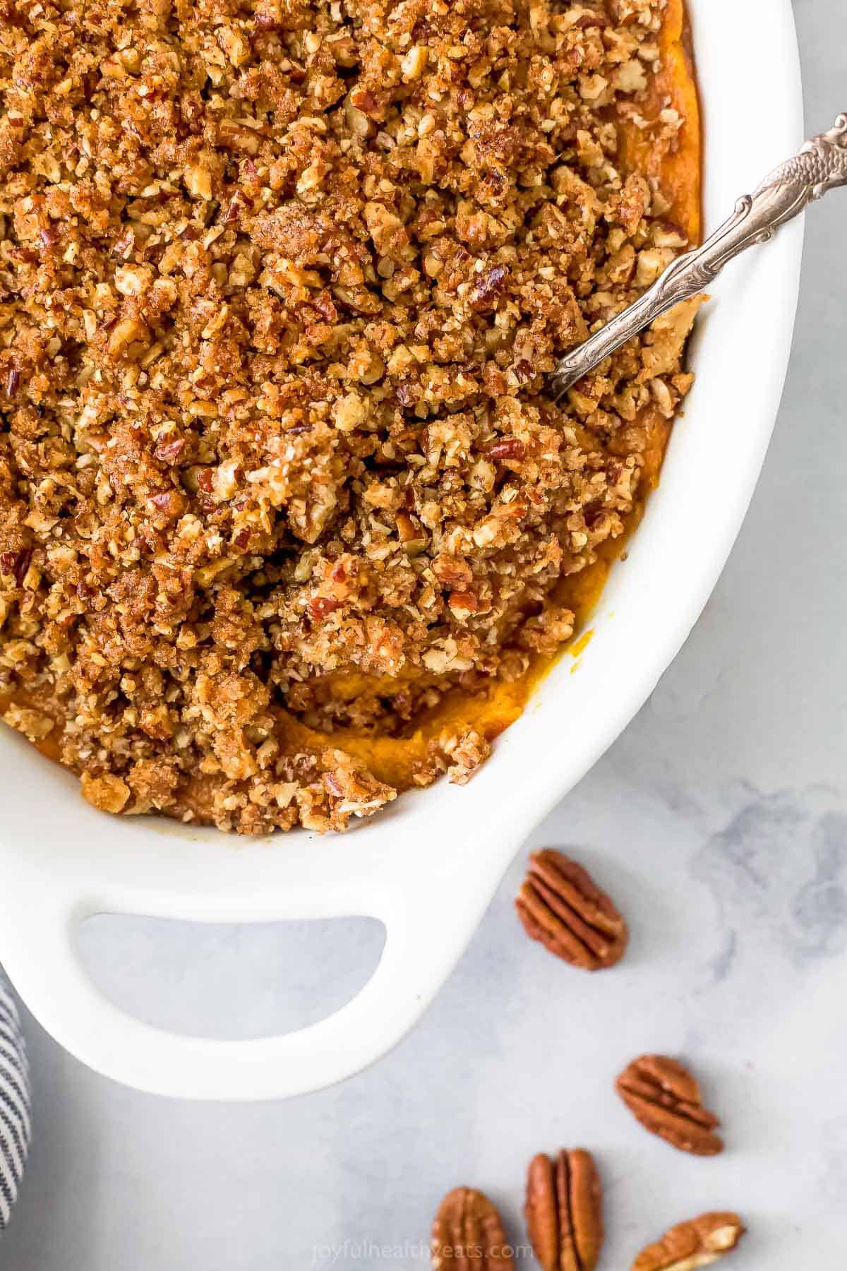 A sweet potato casserole with a crunchy pecan topping on a marble countertop