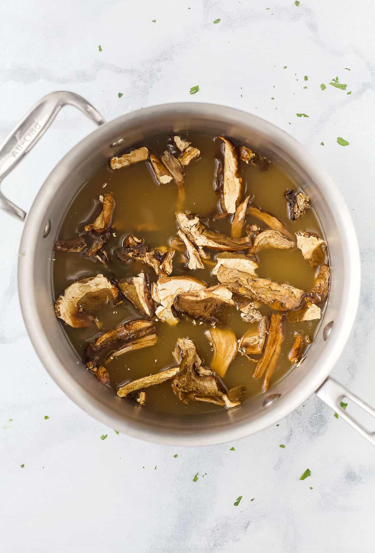 A saucepan filled with broth and dried porcini mushrooms