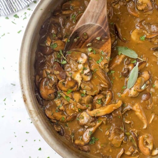 Homemade brown gravy in a pan on a countertop beside a striped dish towel