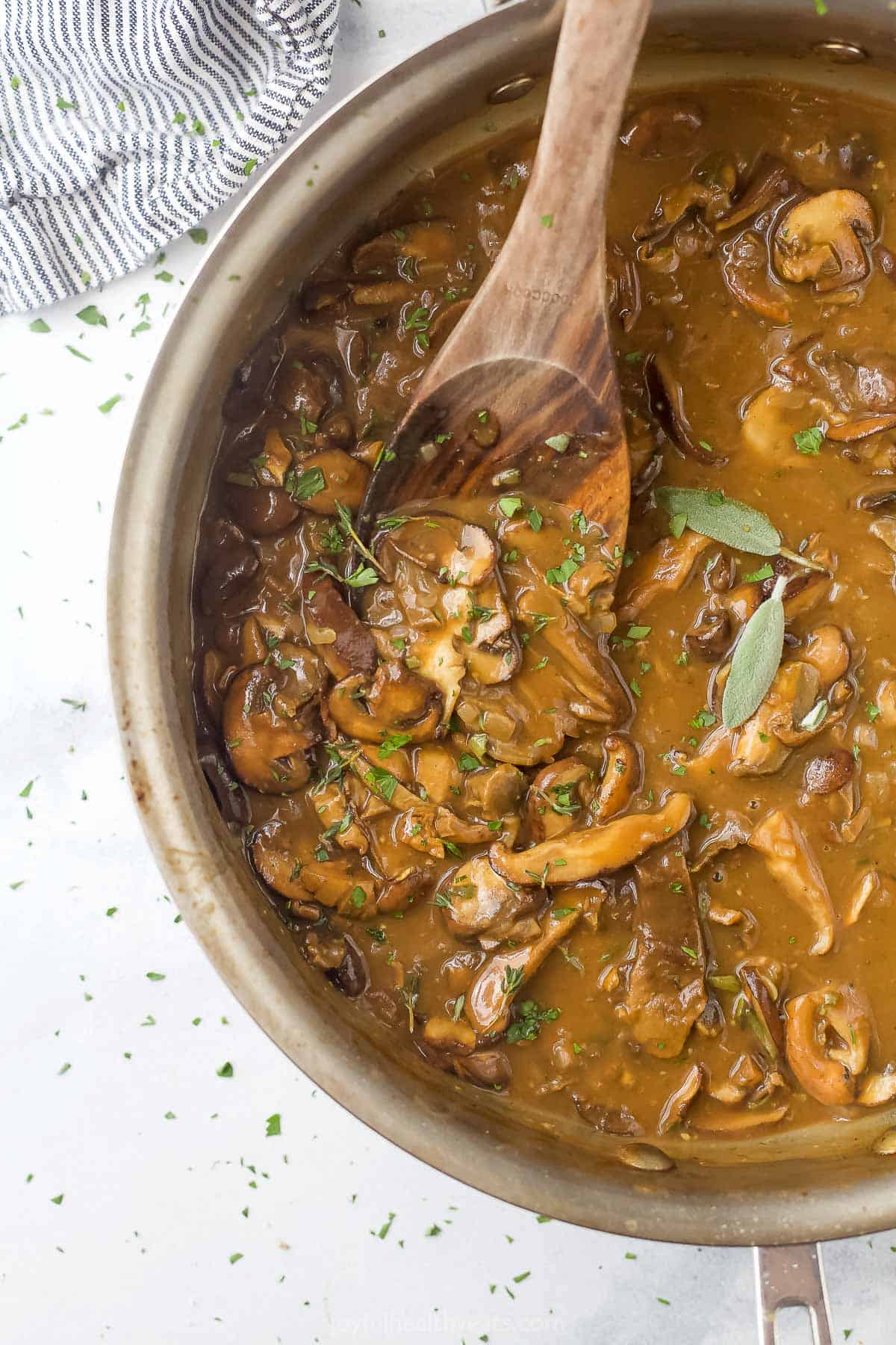 Homemade brown gravy in a pan on a countertop beside a striped dish towel