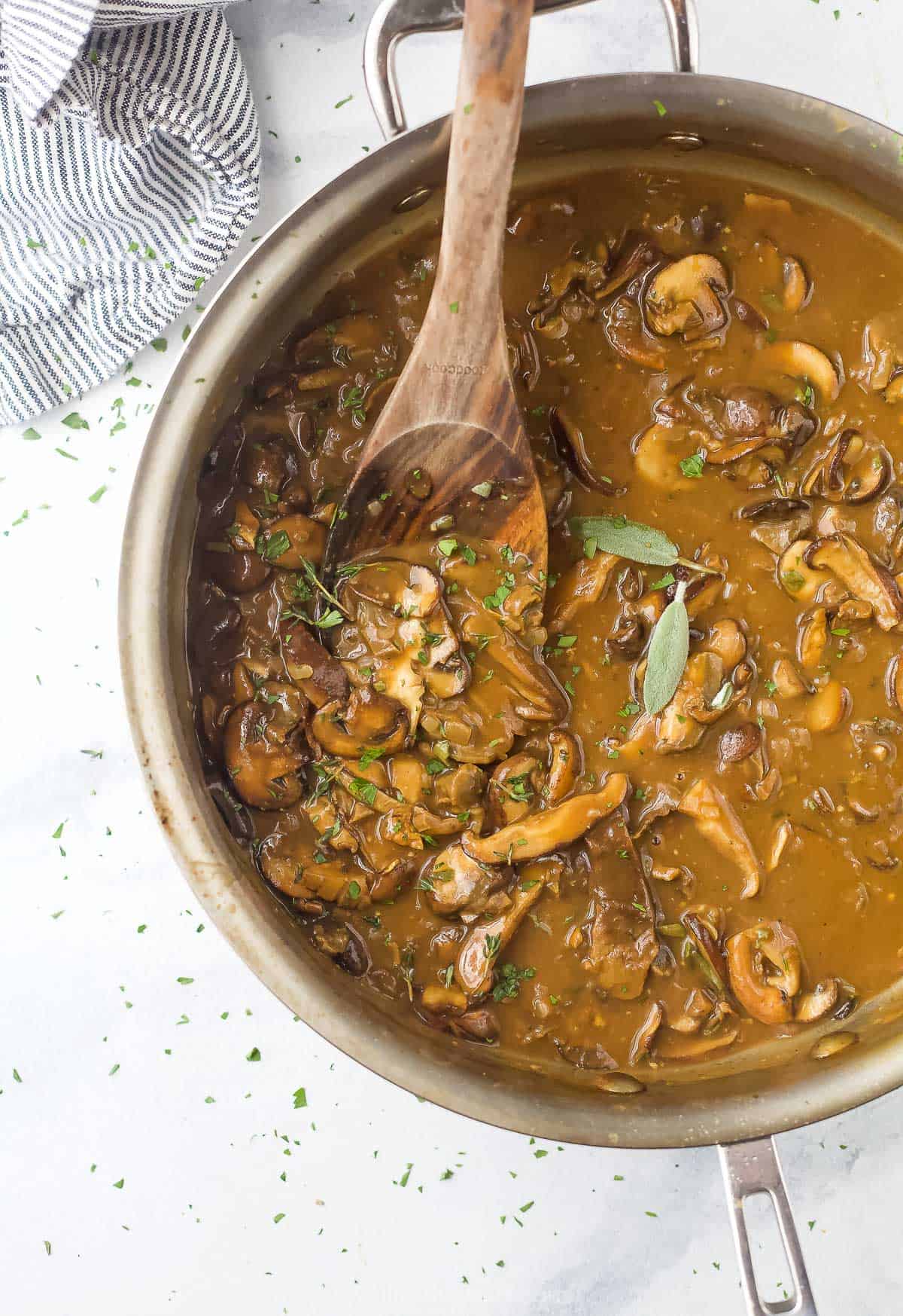 A bowl of gravy on a countertop being stirred with a large spoon