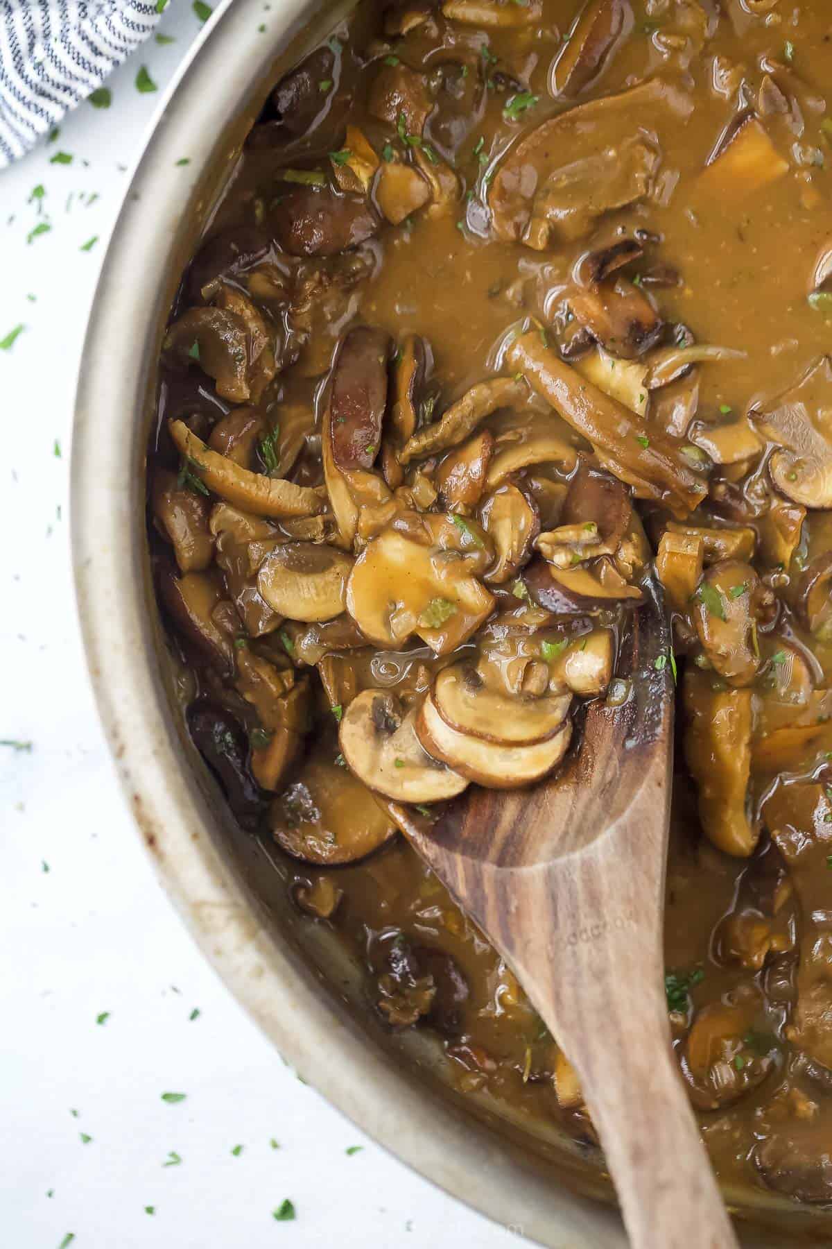 Mushroom gravy inside of a metal pot with a wooden spoon