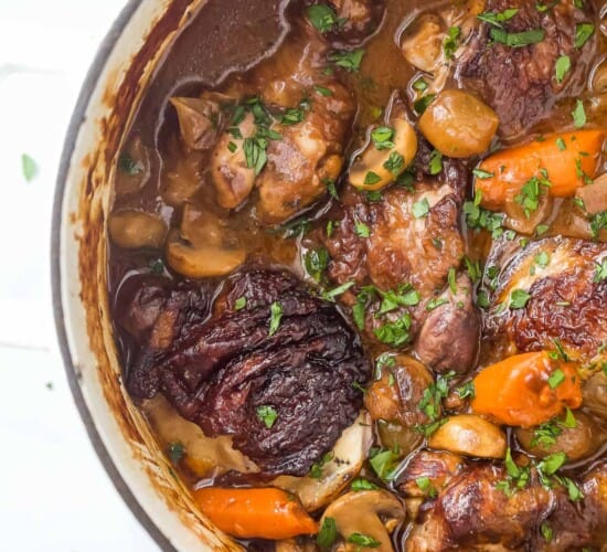 A dutch oven full of chicken stew garnished with finely chopped herbs on a countertop