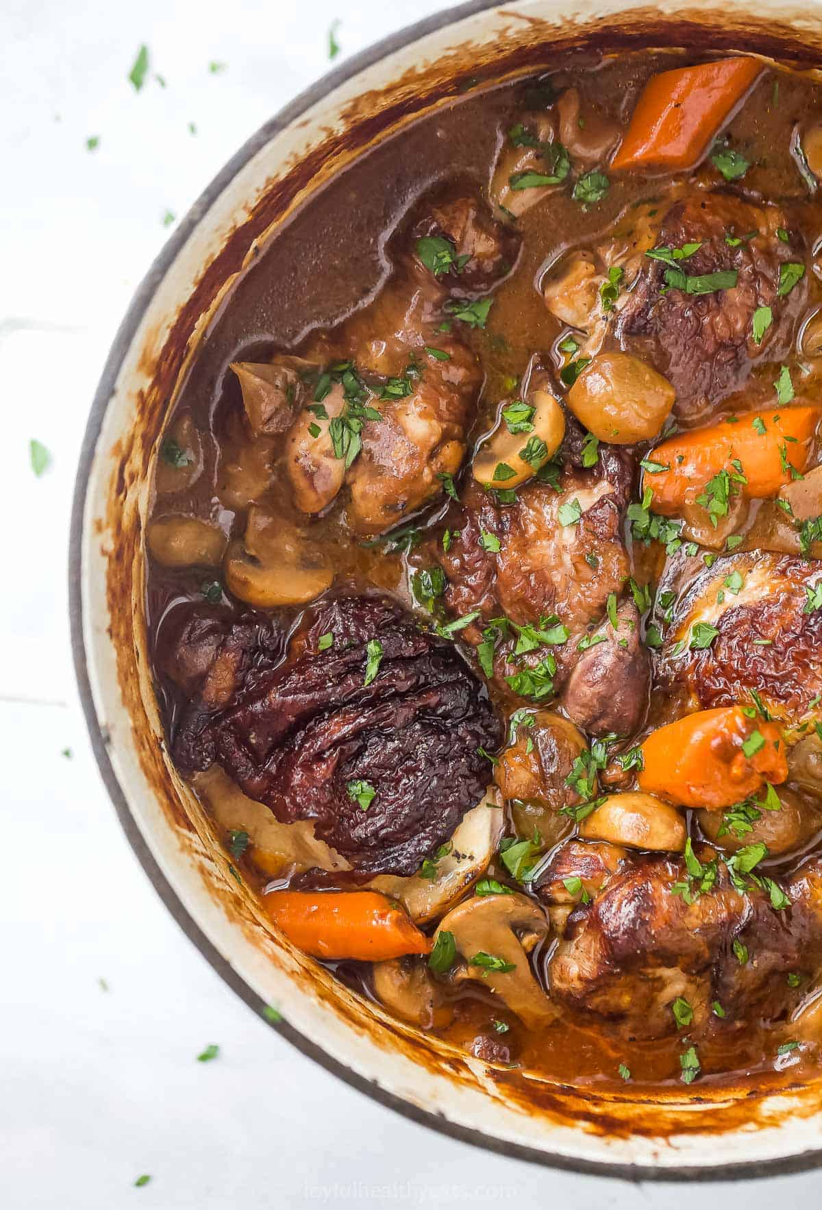 A dutch oven full of chicken stew garnished with finely chopped herbs on a countertop