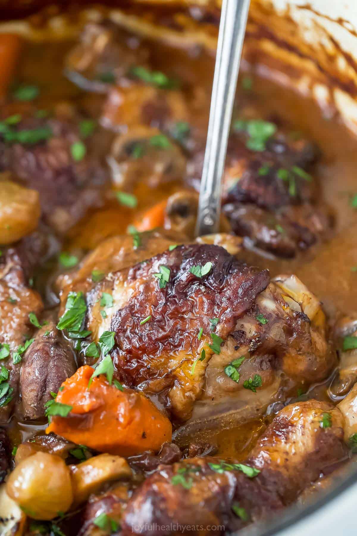 A large pot containing coq au vin stew being stirred with a metal ladle