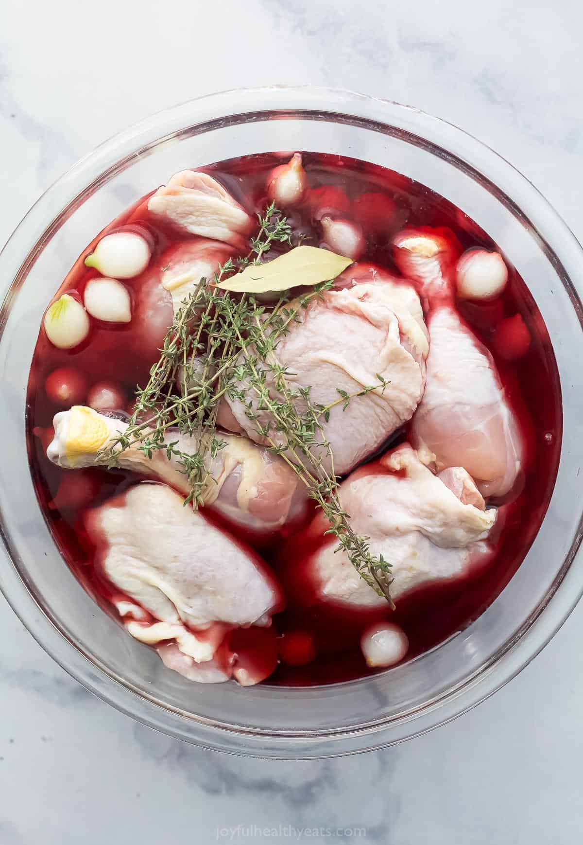 Chicken thighs and drumsticks in a large glass bowl with pinot noir, fresh thyme and pearl onions