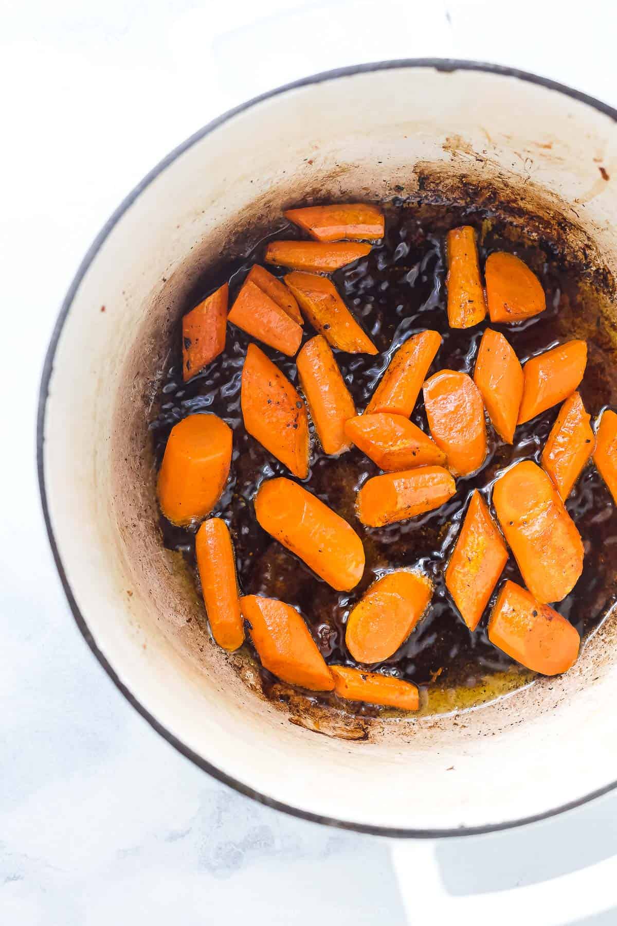 Carrots sautéing in a white dutch oven with a blue rim