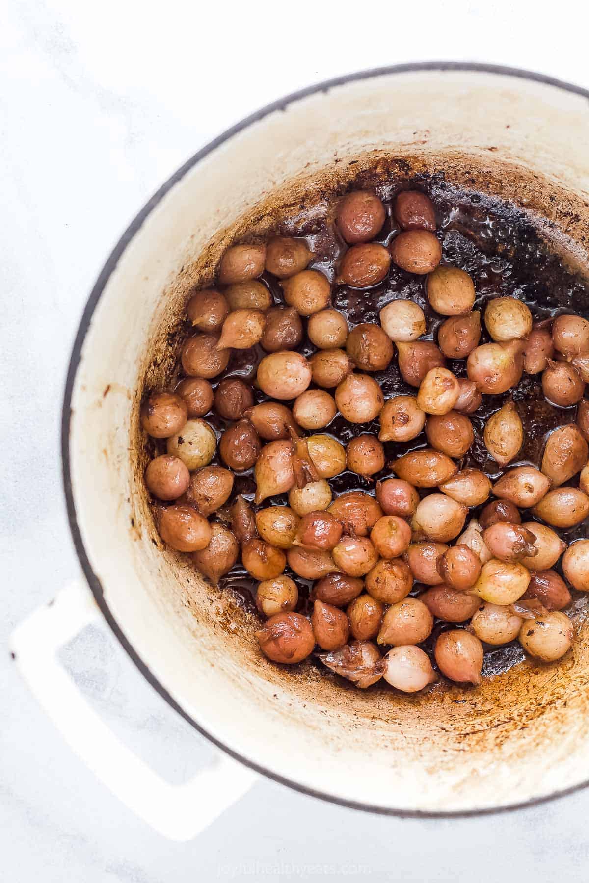 Pearl onions cooking inside of a large dutch oven with handles