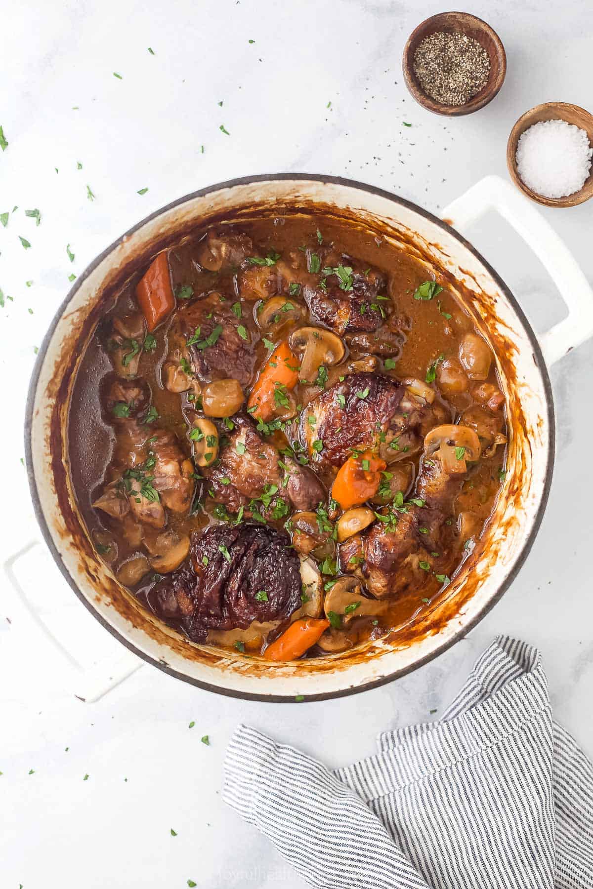 A pot of coq au vin stew on a granite counter with salt and pepper beside it