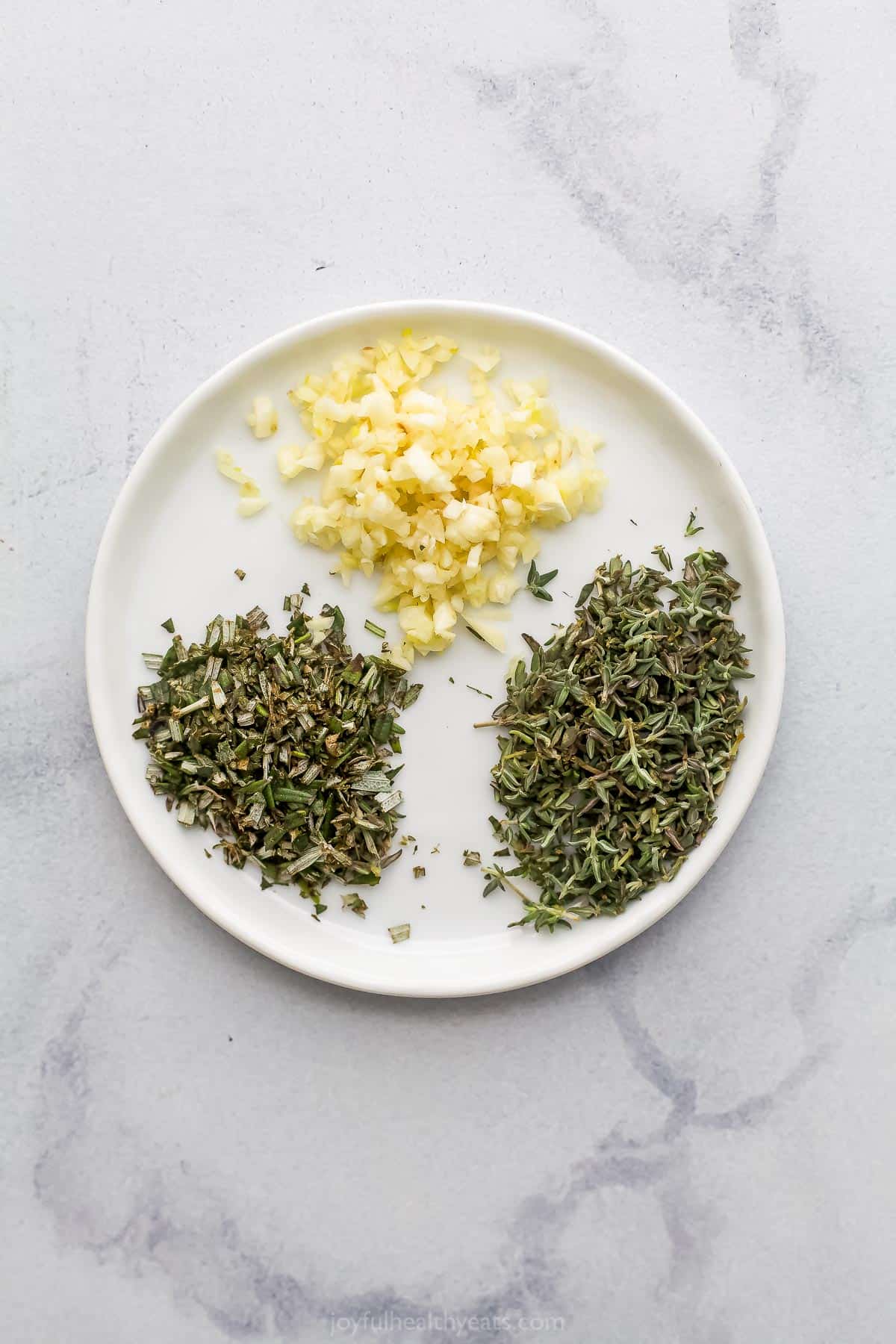 Minced garlic, chopped thyme and chopped rosemary on a white plate