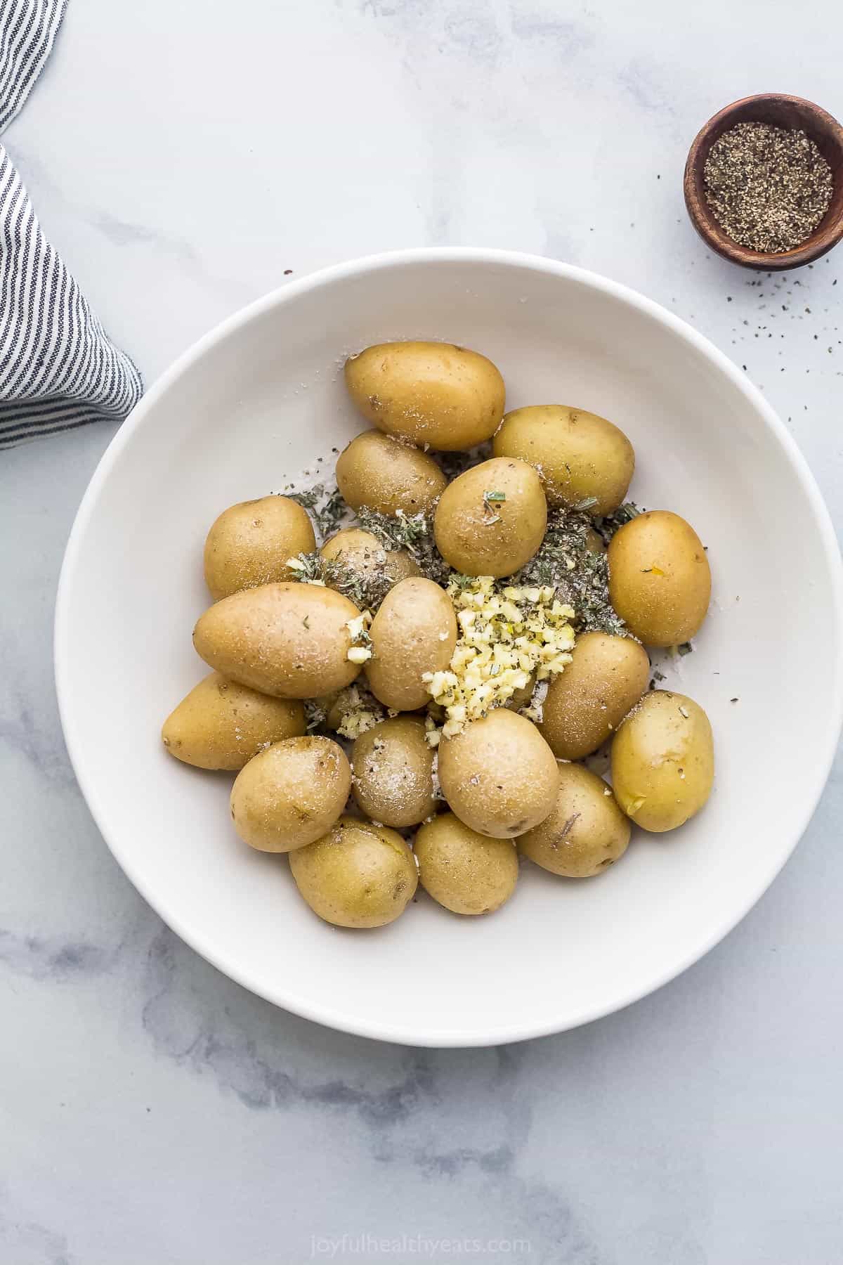 Mini yellow potatoes in a bowl with the seasonings beside a dish of salt and pepper