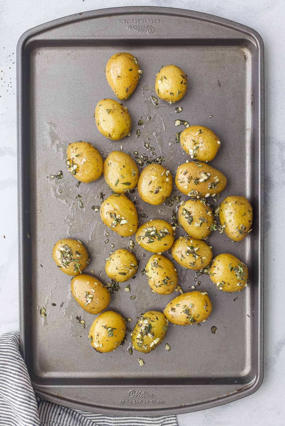 Seasoned, unbaked potatoes on a baking sheet beside a striped dishtowel