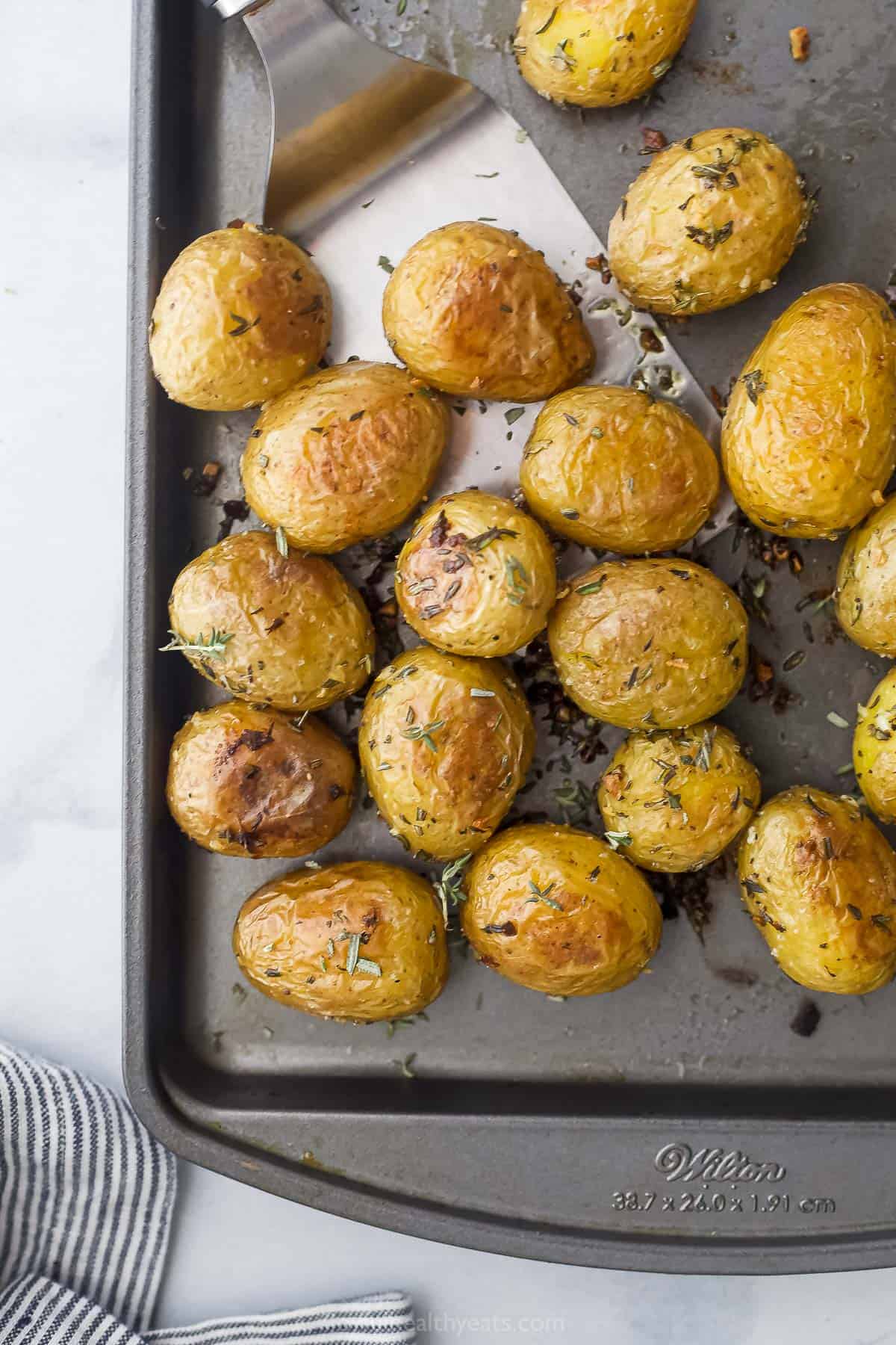 A metal spatula lifting up some crispy oven-baked potatoes from a baking sheet