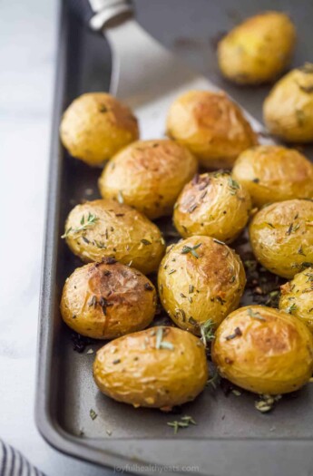 A close-up shot of crispy oven-baked garlic herb potatoes on a metal baking sheet