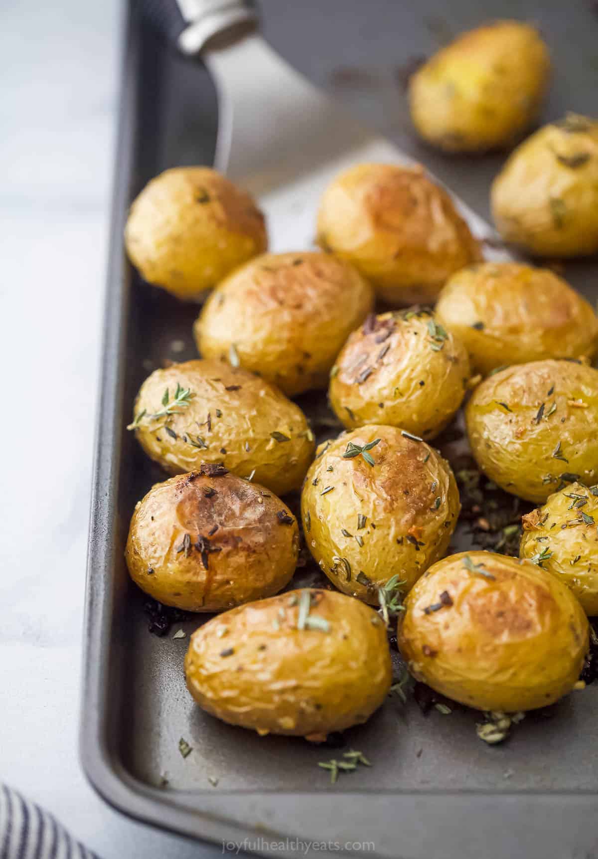 A close-up shot of crispy oven-baked garlic herb potatoes on a metal baking sheet