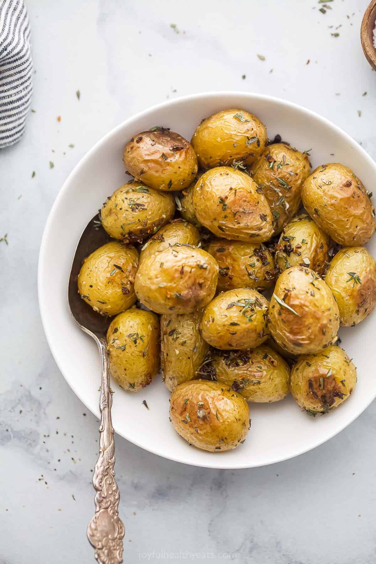 A large bowl filled with mini garlic herb roasted potatoes on a granite countertop