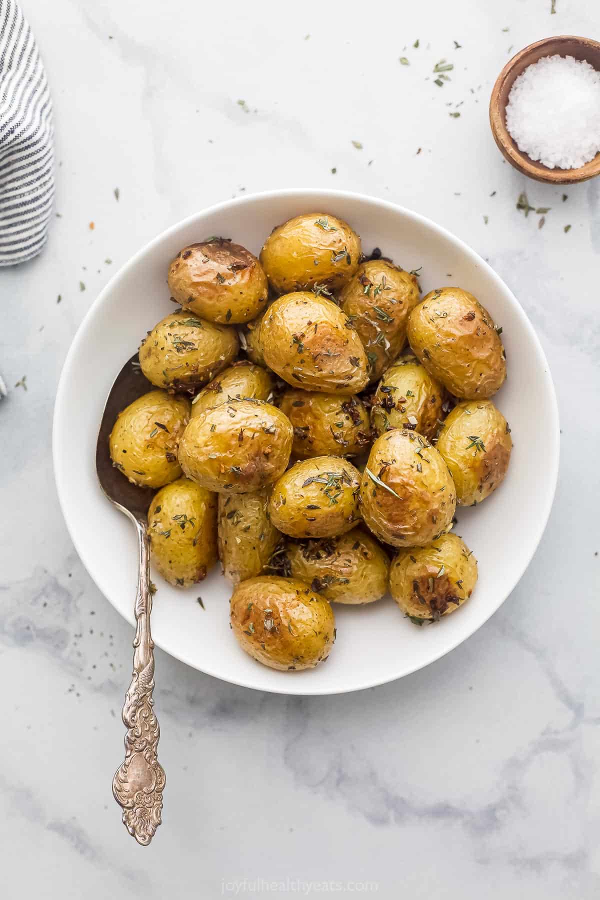 A batch of garlic herb potatoes in a shallow bowl with a metal spoon inside