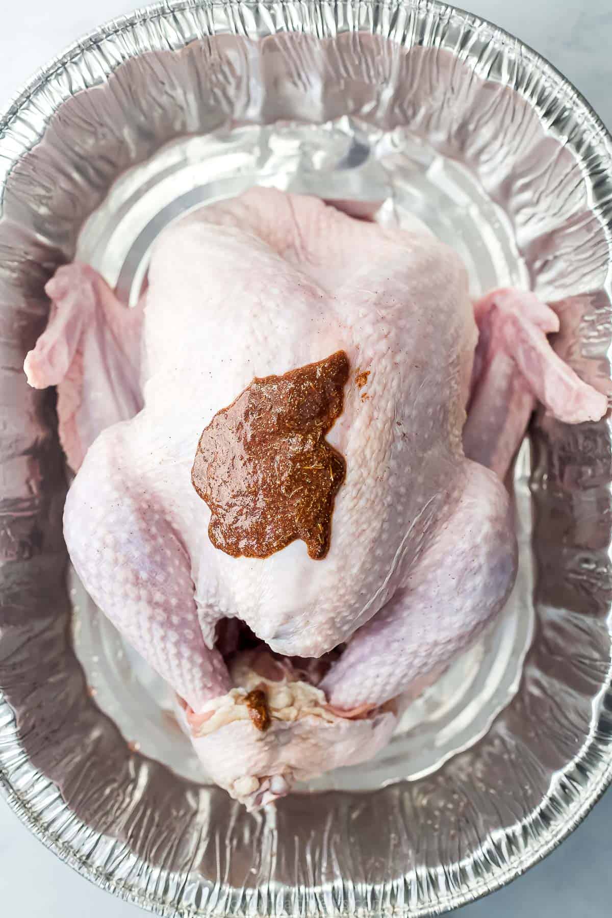 maple spice rub on a raw turkey in a roasting pan