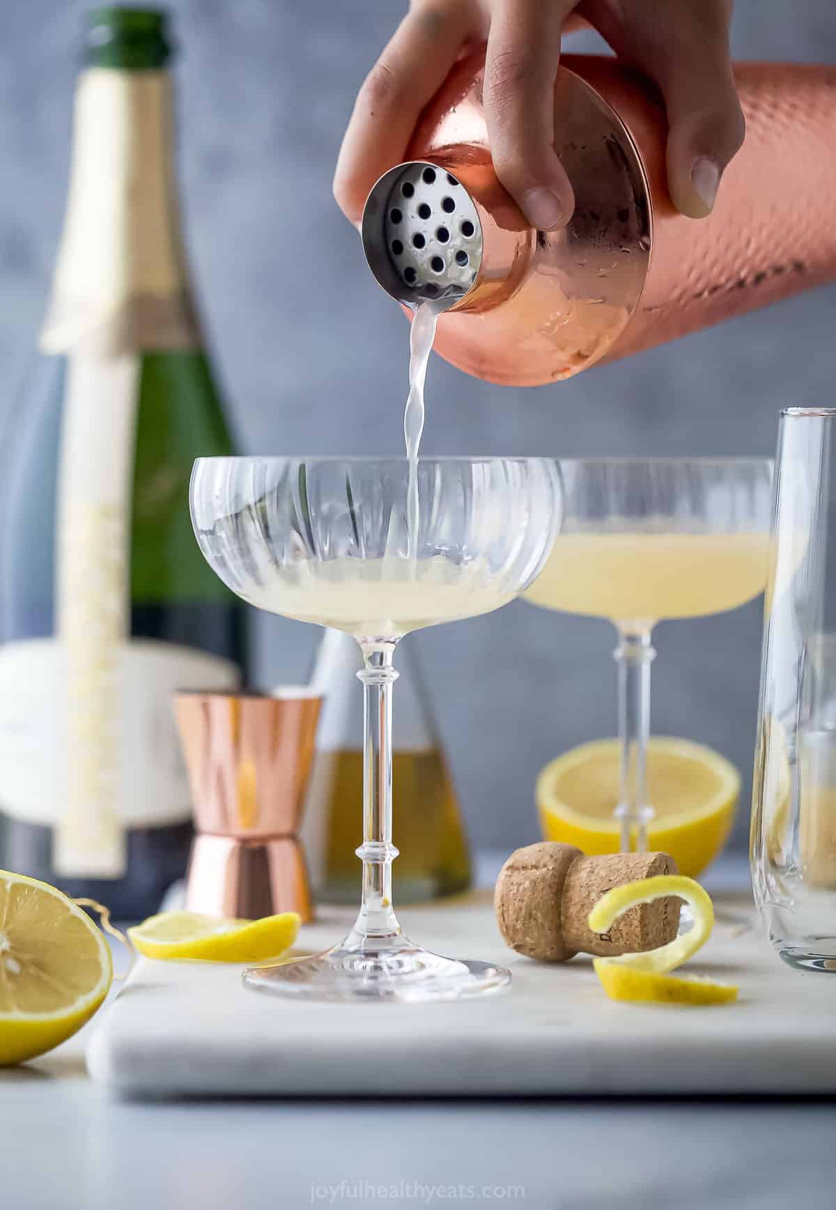 A mixed drink being poured from a copper cocktail shaker to a tall champagne glass