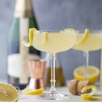 Two classic French 75 cocktails on a surface cluttered with a bottle of champagne and fresh lemon slices