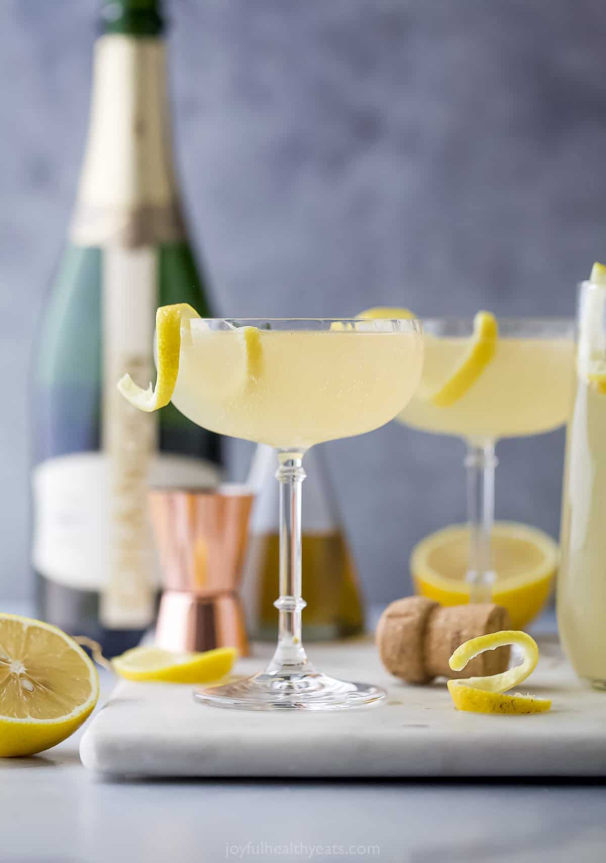 Two lemon gin cocktails on a cutting board with a glass of champagne behind it