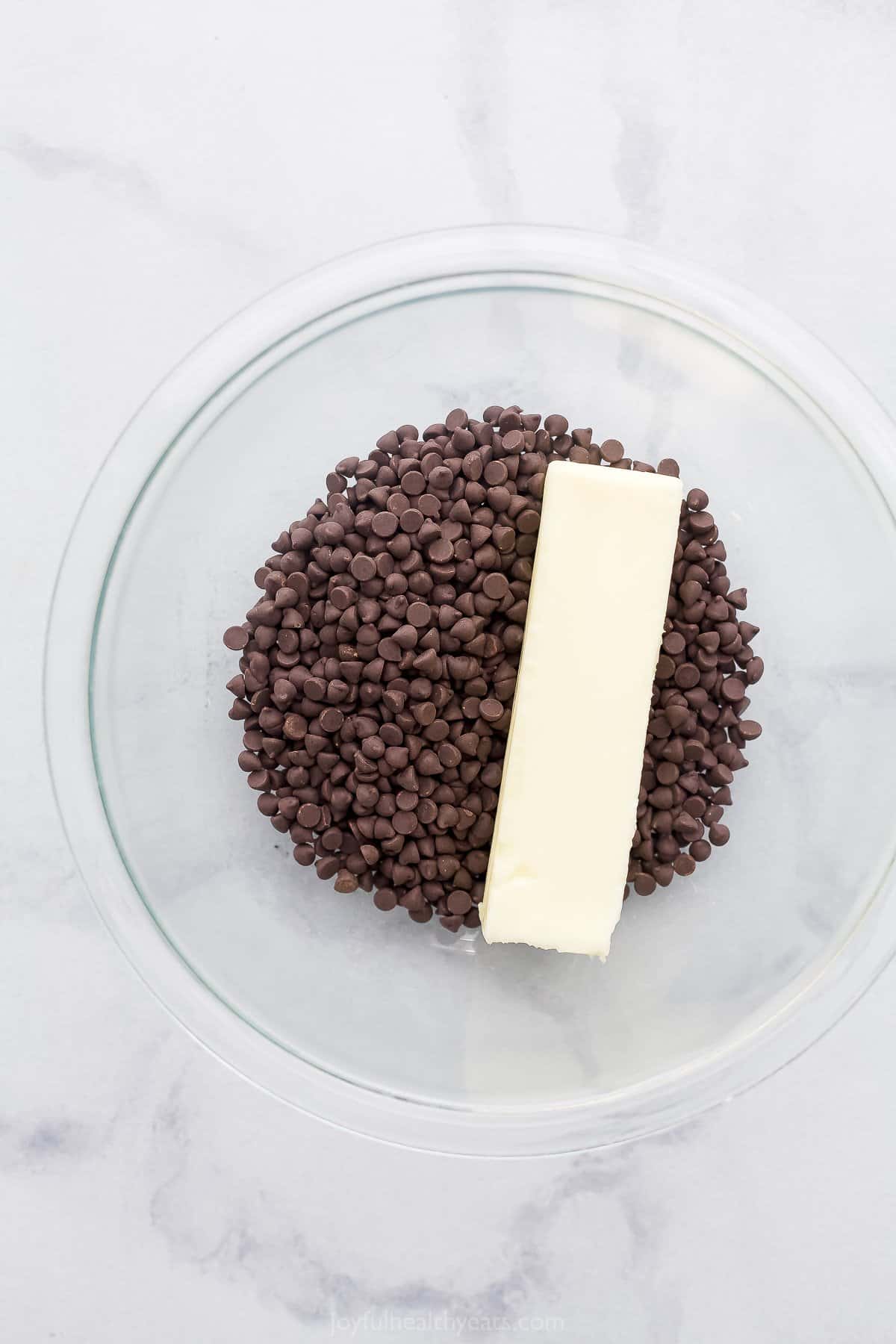 A glass mixing bowl full of semi-sweet chocolate chips and a stick of unsalted butter