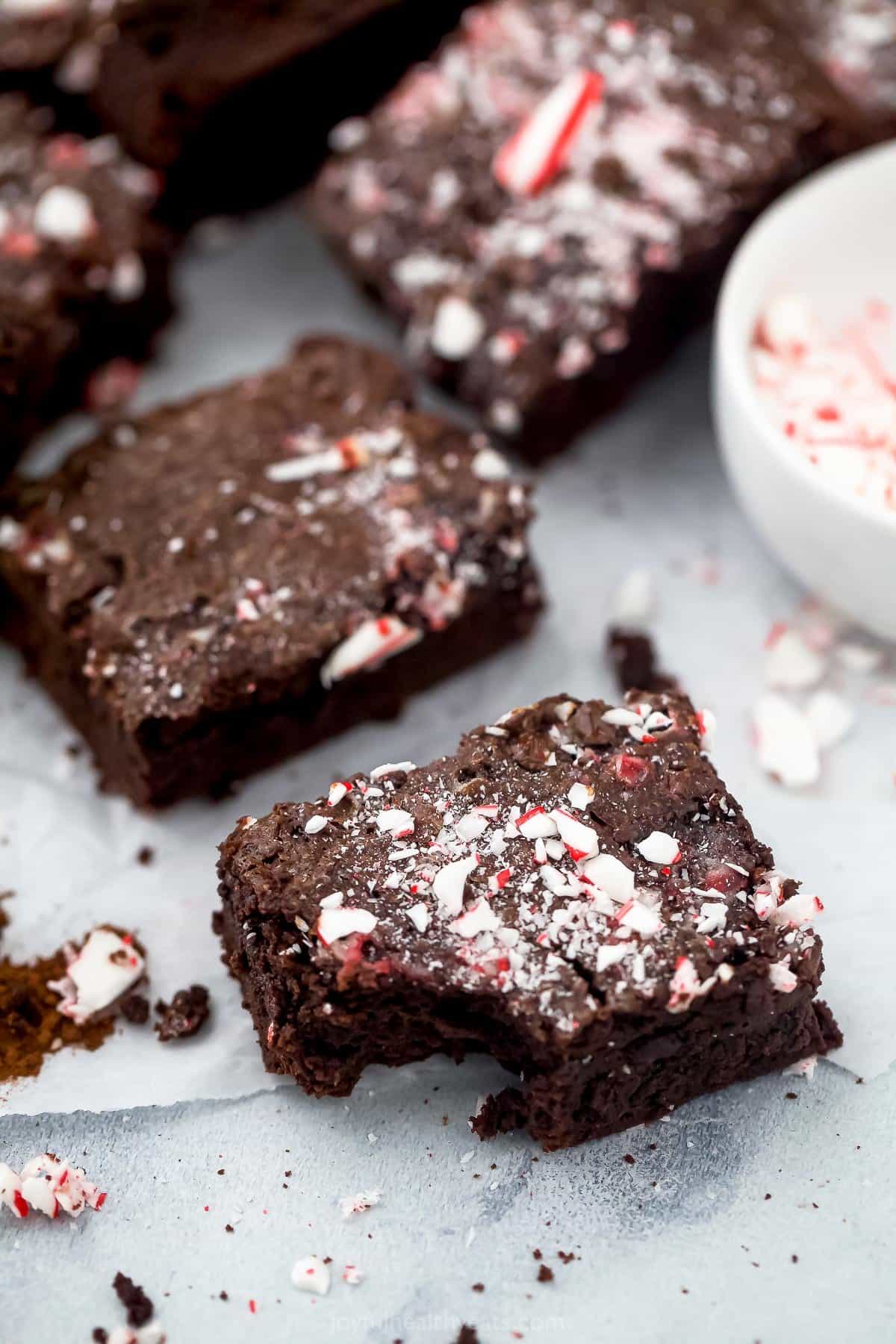 A peppermint brownie with a bite taken out of it beside a bowl of crushed candy canes