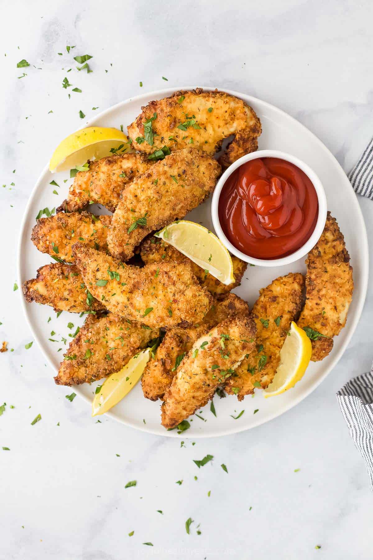 An overhead shot of a plate of homemade chicken strips on a marble countertop