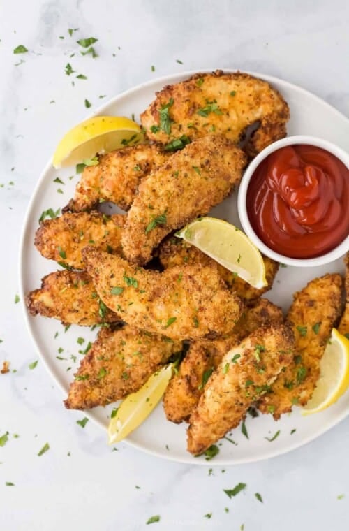 Air Fryer chicken strips on a plate with fresh lemon slices and ketchup