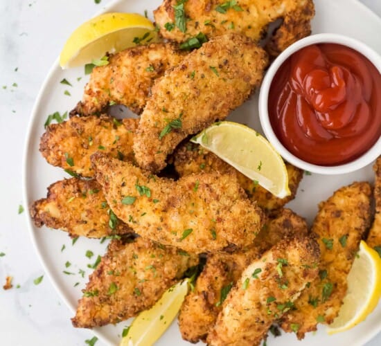 Air Fryer chicken strips on a plate with fresh lemon slices and ketchup