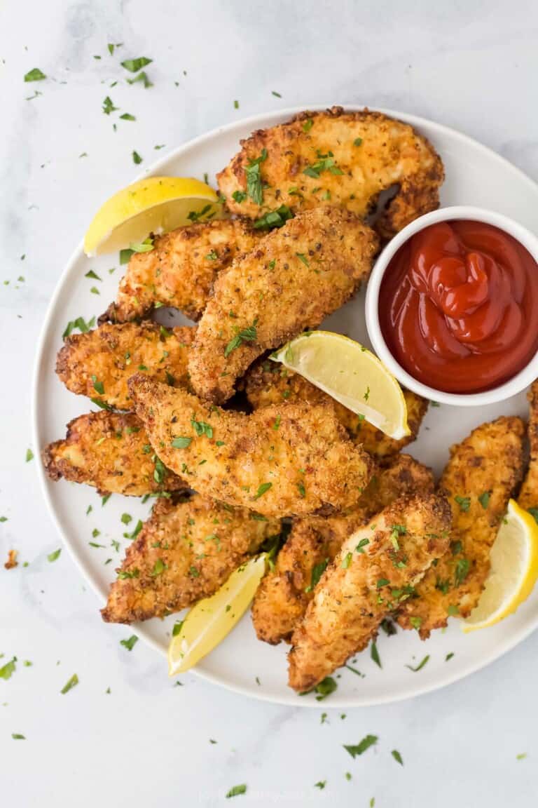 Air fryer chicken strips on a plate with fresh lemon wedges and ketchup