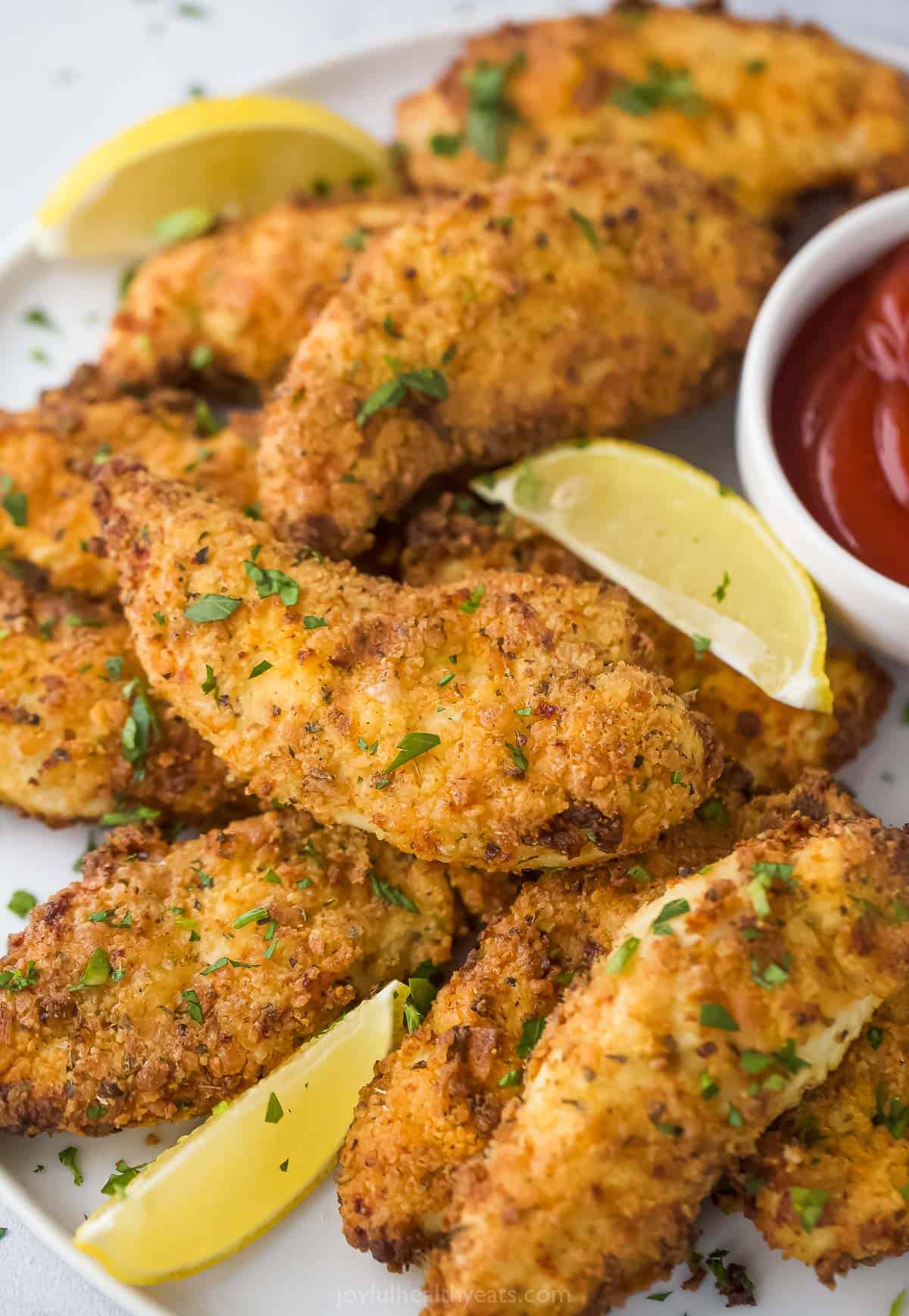 A plate of Air Fryer chicken tenders with three lemon wedges and a sprinkle of chopped parsley