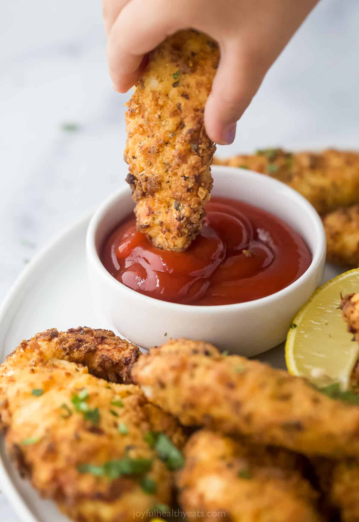 A homemade chicken tender being dunked into a small dish of ketchup