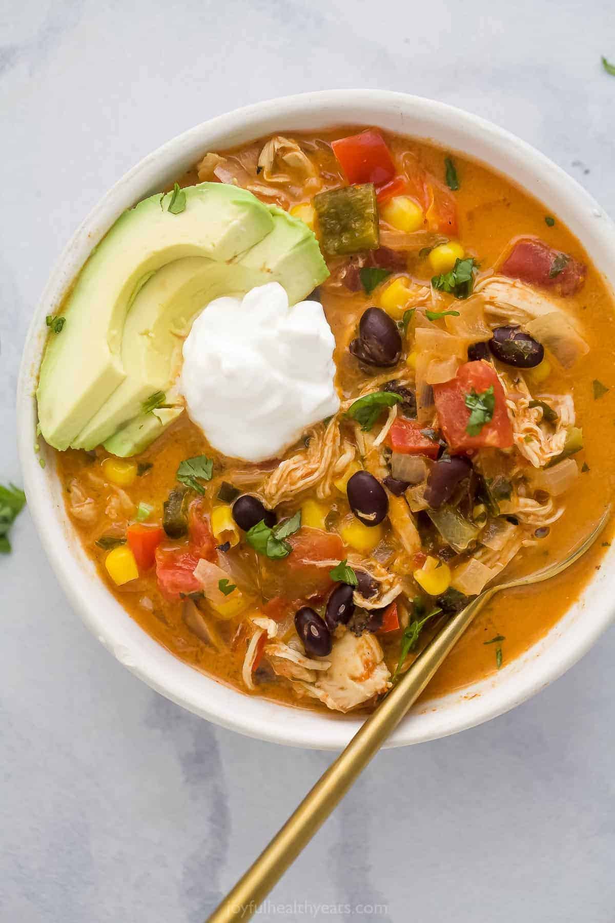 A bowl of chicken enchilada soup topped with sour cream and avocado slices.
