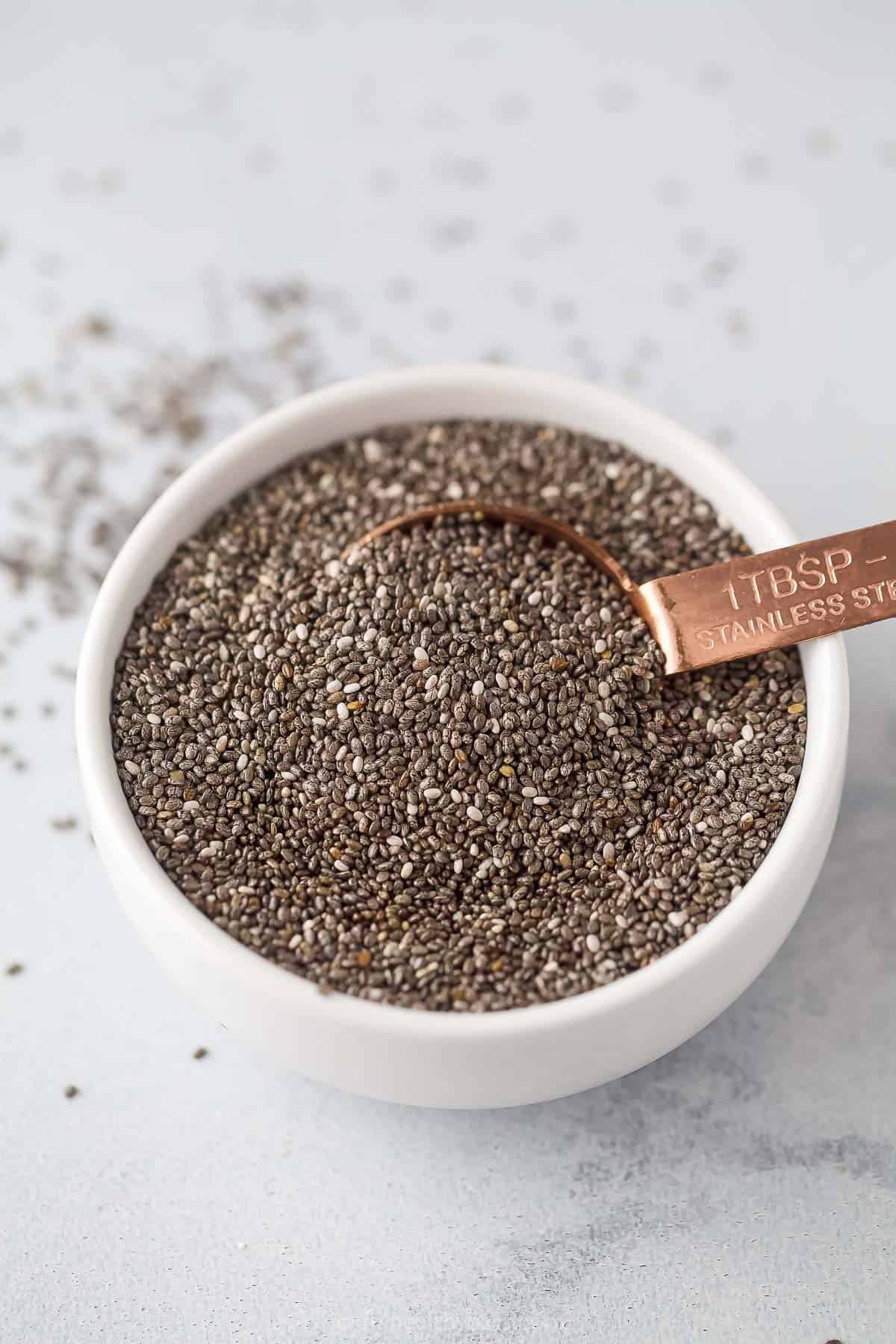 A bowl of chia seeds on a marble countertop with a copper tablespoon digging into it