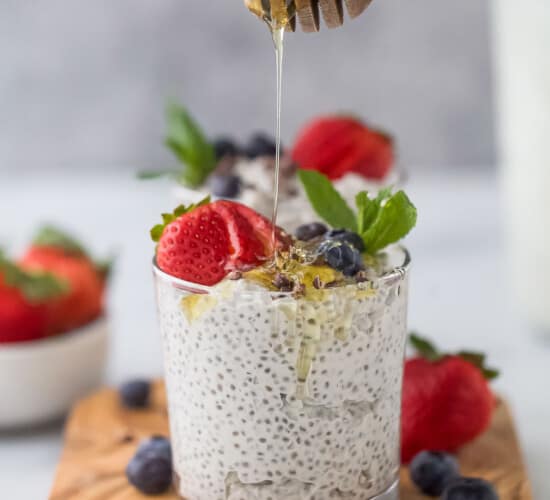 Raw honey being drizzled over a cup of chia seed pudding topped with fresh berries