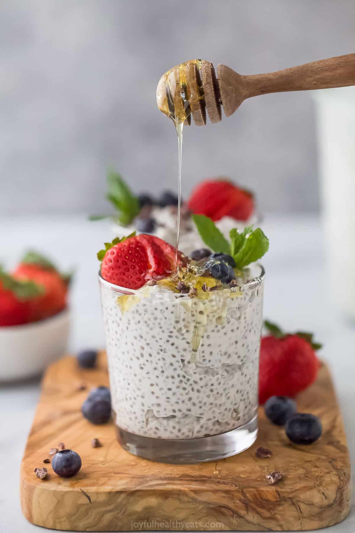 Raw honey being drizzled over a cup of chia seed pudding topped with fresh berries