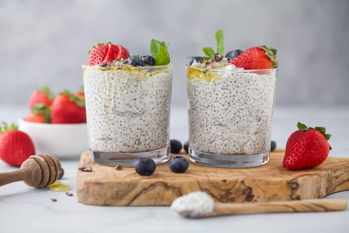 Two cups of creamy chia seed pudding sitting side by side on a wooden slab