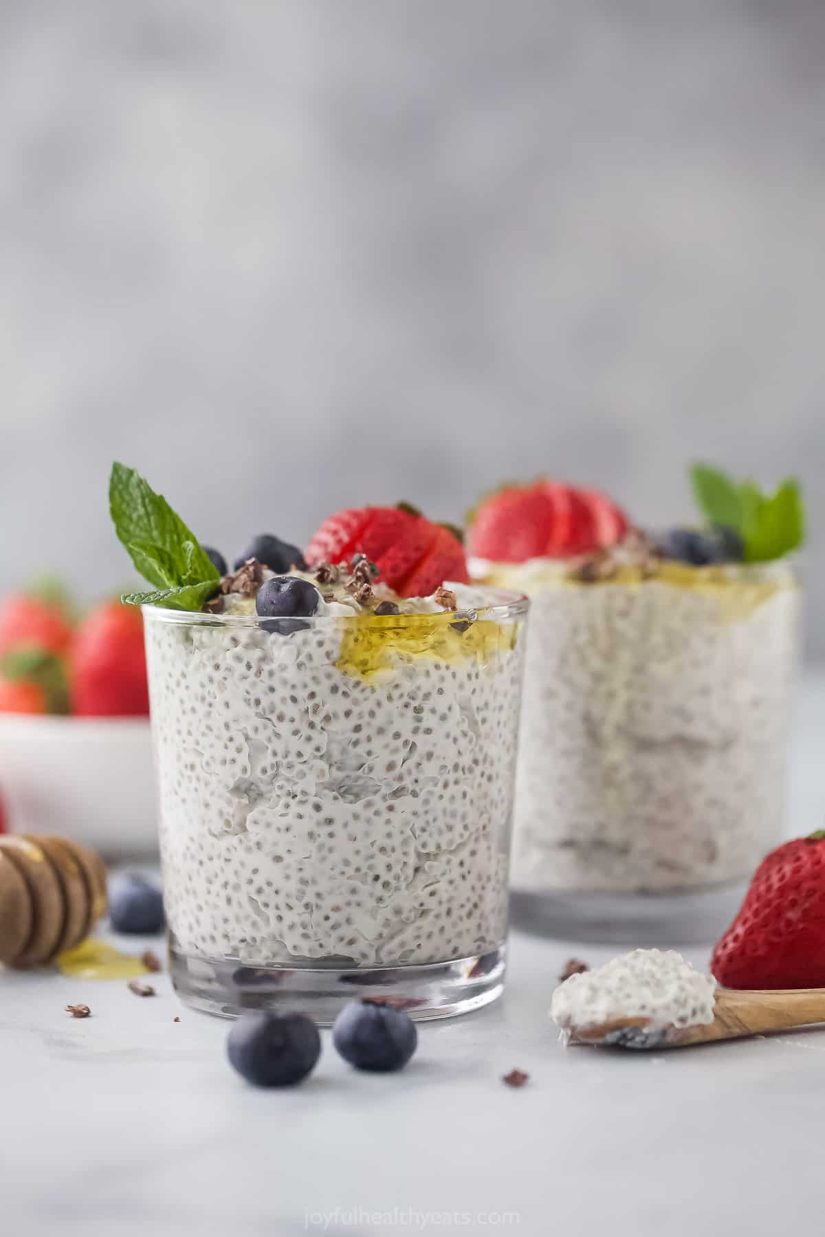 A glass of chia pudding garnished with a mint leaf in front of a second glass of pudding on a countertop