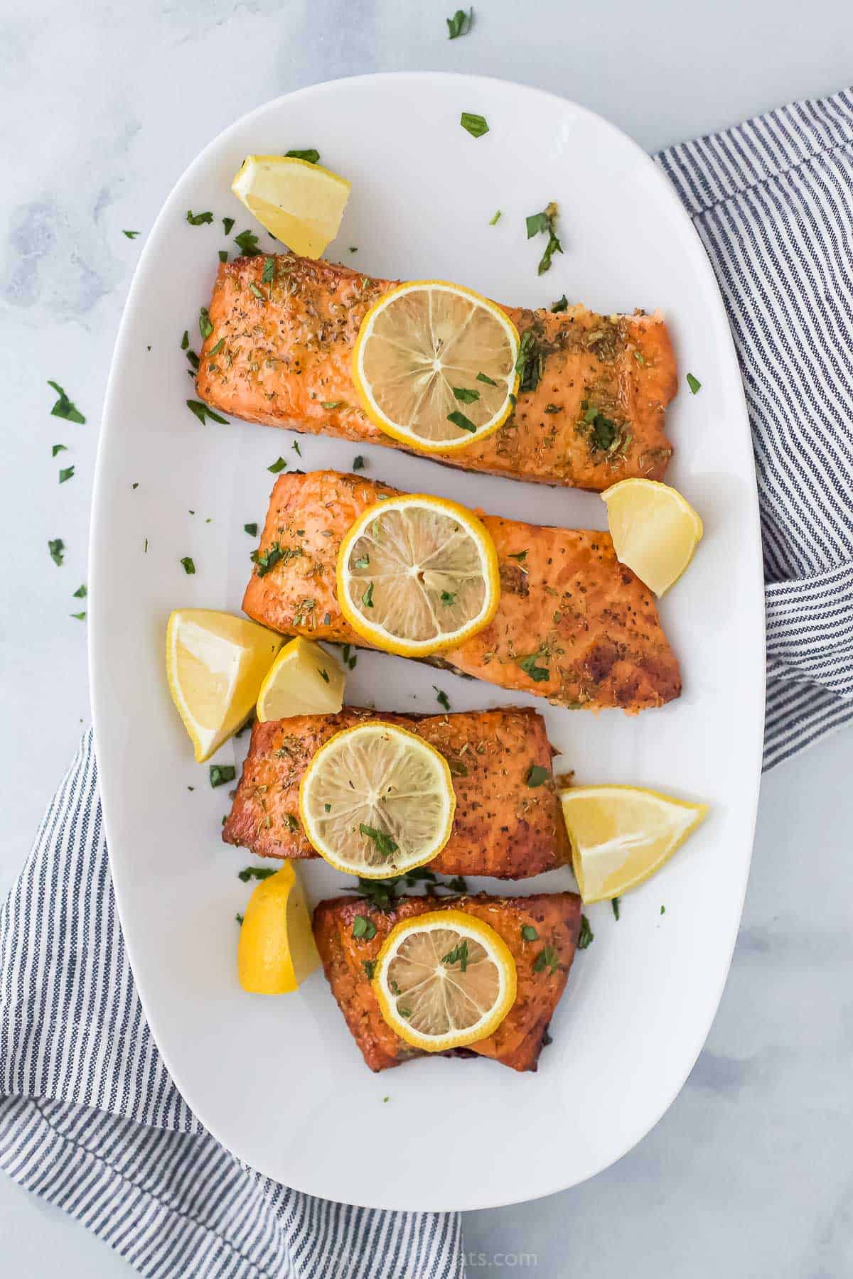 A white plate with 4 fillets of salmon cooked in air fryer, topped with lemon.