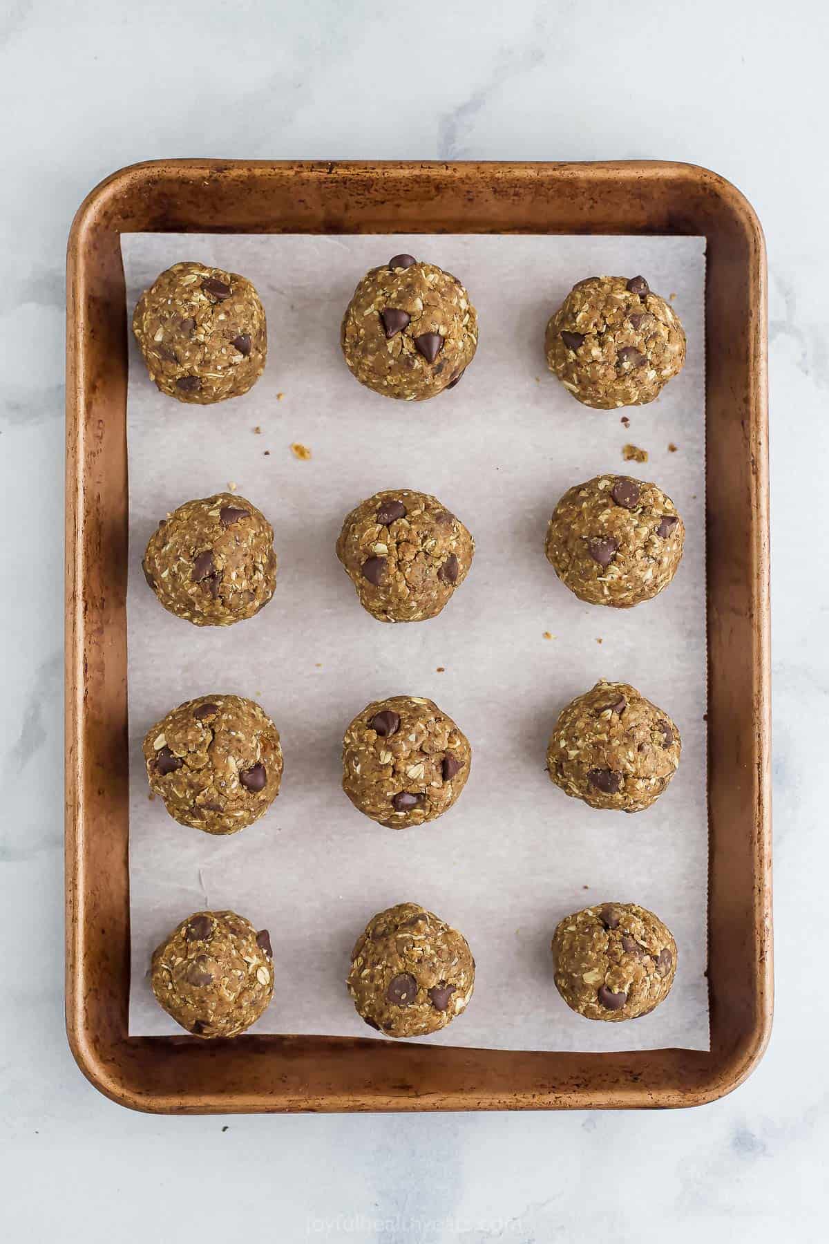 Twelve peanut butter chocolate chip protein balls evenly spaced on a baking sheet lined with parchment paper