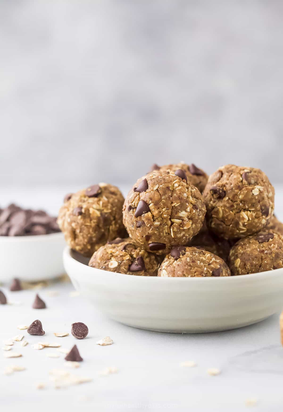 A bowl of peanut butter protein balls on a countertop beside a dish of mini chocolate chips