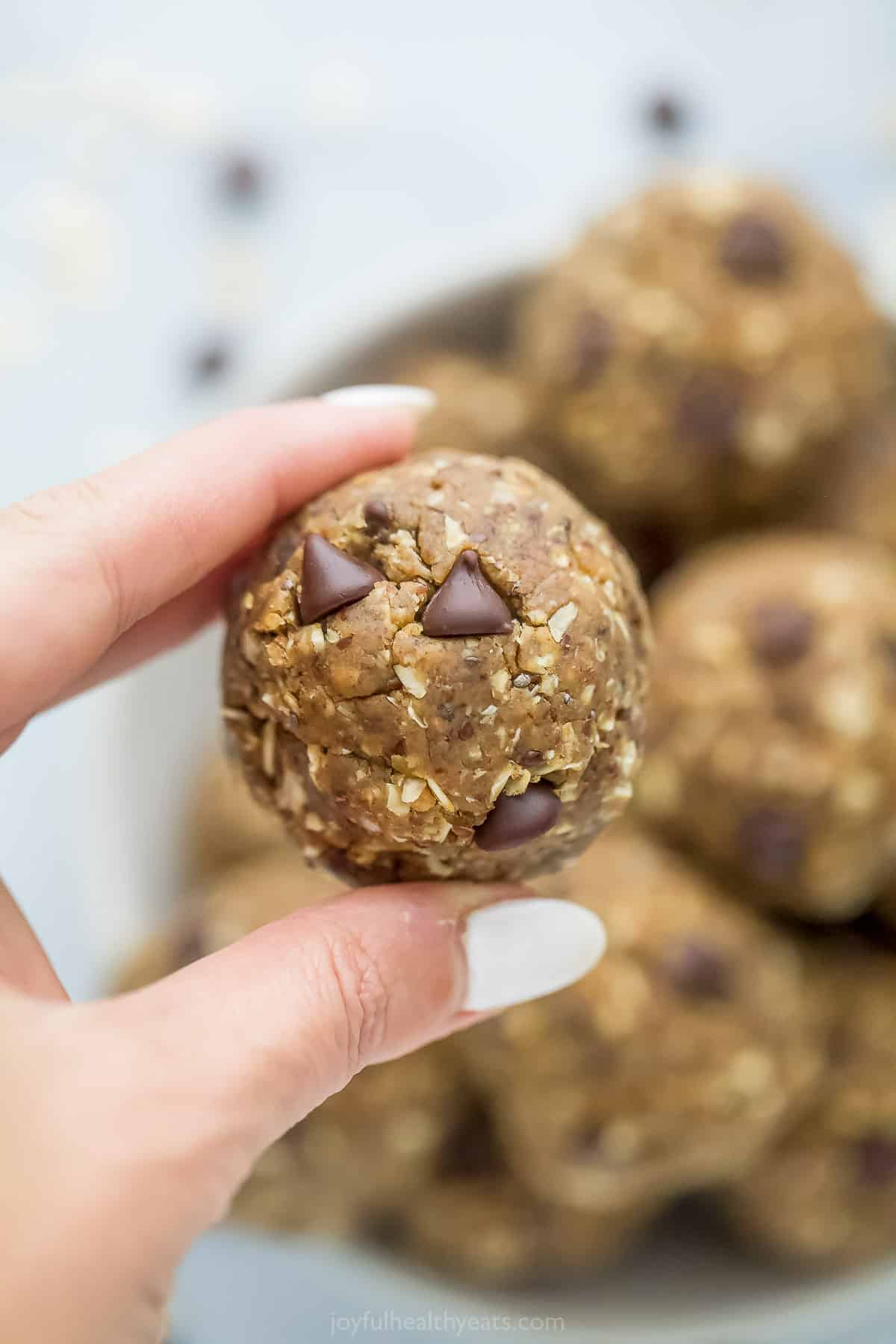 A peanut butter chocolate chip protein bite being held above a bowl full of additional energy balls